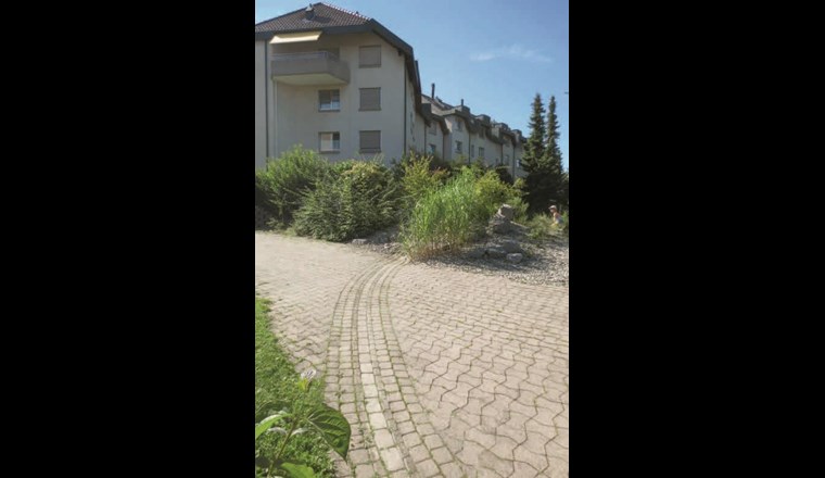 Siedlung «Im Park» in Ittigen bei Bern: Umgebungsgestaltung mit durchlässigen Oberflächen in Form von Kies, Rasen und Verbundsteinen. Abführung des Dachabwassers mit oberflächlicher Wasserführung. Das Dachwasser wird soweit möglich über die Kiesfläche versickert und der Überlauf wird oberflächlich in der Rinne bis zu einer zentralen Versickerungsanlage abgeführt.