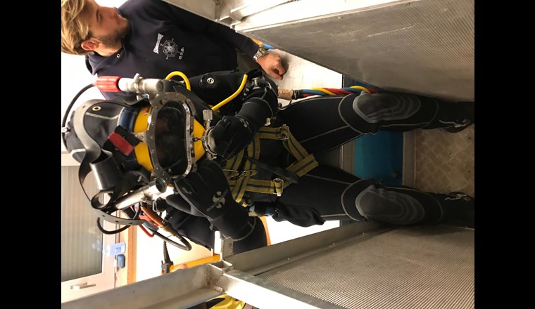 Der Taucher mit dem Tauchanzug begibt sich mit einer Kabine ins Wasser.