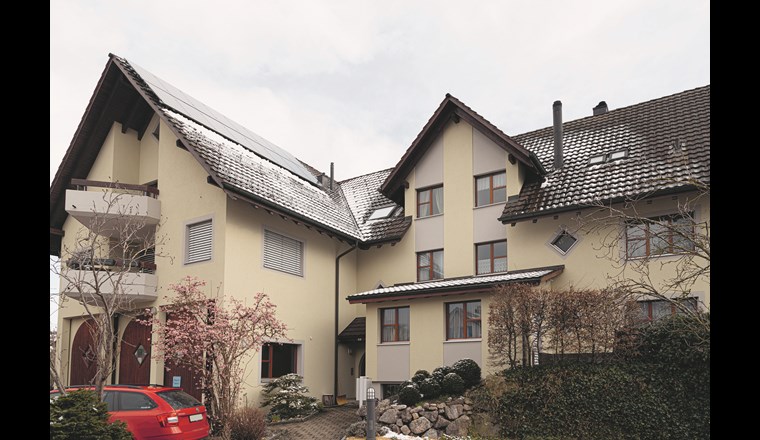 Der Hauseingang des Mehrfamilienhauses mit der
auf dem Dach installierten PV-Anlage. (Quelle Hoval AG)
