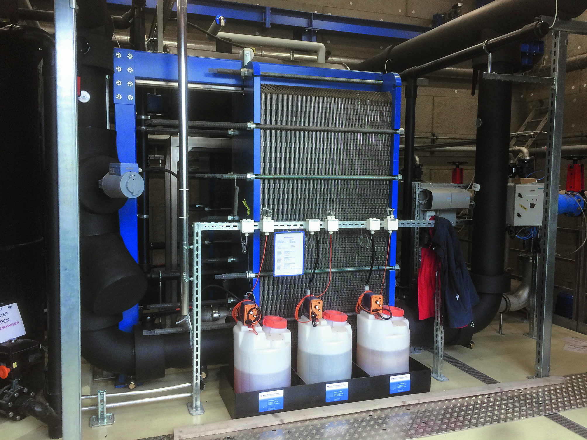 Plattenwärmetauscher und Reinigungsanlage. Im Vordergrund sind die Reinigungs- und Desinfektionsflüssigkeiten für die automatische Spülung der Wärmetauscher zu sehen.